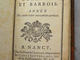 Quelqu'un tient à la main un livre sur lequel figure une image représentant des armoiries.