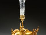 un vase en or orné d'un oiseau et surmonté d'un autre oiseau