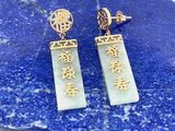 une paire de boucles d'oreilles ornées d'inscriptions en chinois, posée sur une plaque de marbre bleu