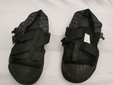 pair of black sandals on a bed with a white sheet