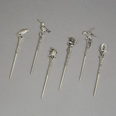 cinq cuillères en argent ornées d'oiseaux et de fleurs, posées sur une table