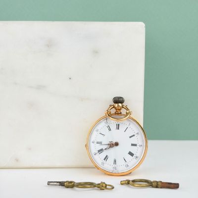 une montre de poche ancienne posée sur un bloc de marbre à côté d'une paire de ciseaux