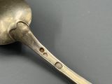 une cuillère en argent percée de trous posée sur une surface grise