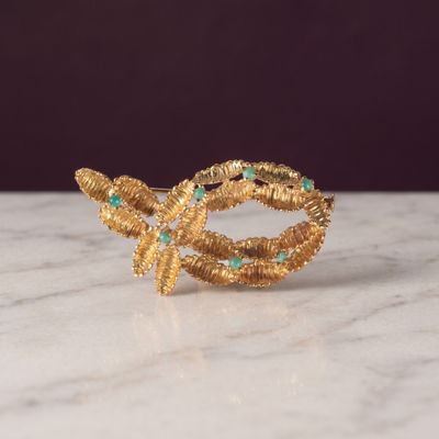 un gros plan d'une bague en or sertie de pierres vertes posée sur une surface en marbre