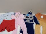 Plusieurs vêtements pour bébés sont disposés sur une table blanche