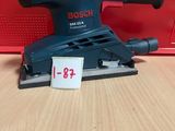 un gros plan d'une ponceuse posée sur une table, avec une boîte rouge en arrière-plan