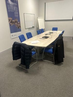 une photo d'une salle de conférence avec des chaises bleues et un écran de projection