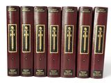 six livres rouges aux tranches dorées sont alignés sur une surface blanche