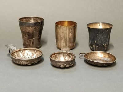 Plusieurs tasses et cuillères en argent sont alignées sur une surface grise