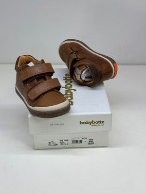 des chaussures de bébé en cuir marron avec des bandes Velcro, posées sur une boîte blanche