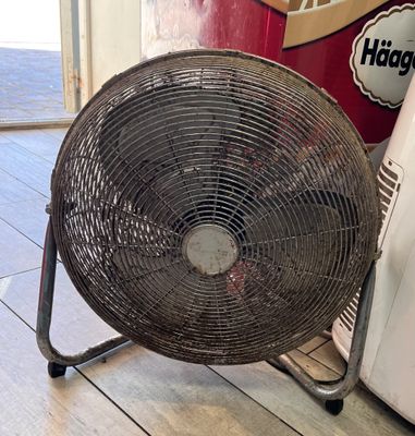 un ventilateur posé par terre à côté d'un réfrigérateur