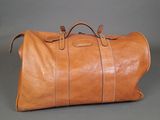 an image of a brown leather duffel bag sitting on a gray surface