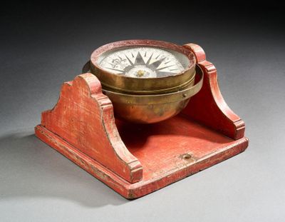 une boussole ancienne en laiton posée sur un socle en bois, elle-même posée sur une surface grise