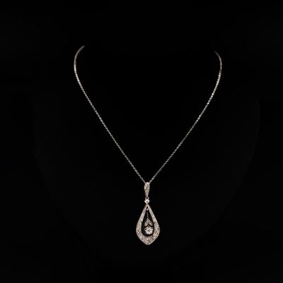 un collier en or blanc orné d'un pendentif en forme de larme serti d'un diamant, sur fond noir