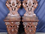 une paire de chaises anciennes en bois sculpté sur des socles, devant un fond bleu
