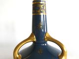 un vase bleu orné de motifs dorés sur un fond blanc