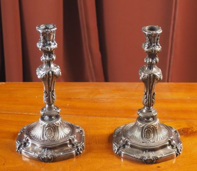 une paire de bougeoirs en argent posés sur une table en bois, avec des rideaux rouges en arrière-plan