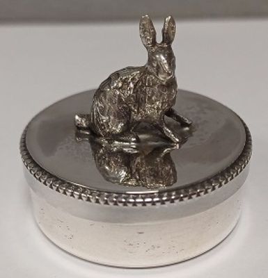 boîte plaquée argent sur laquelle est assis un lapin, posée sur un fond blanc