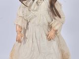 an antique doll with a white dress and bonnet on a wooden stand
