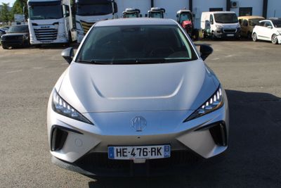 une voiture argentée garée sur un parking, avec des camions en arrière-plan