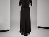 black dress on a mannequin stand in front of a white wall