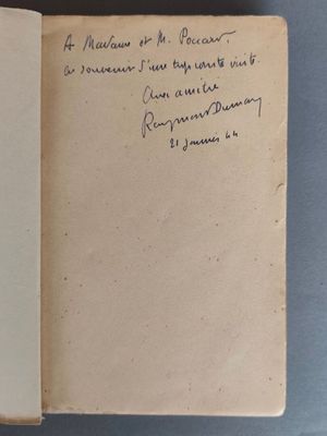 un livre ouvert, sur lequel est posée une note manuscrite, posé sur une table