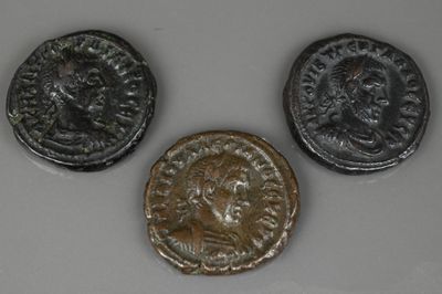 trois pièces de monnaie romaines anciennes posées sur une surface blanche