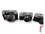 three old cameras are sitting side by side on a white surface