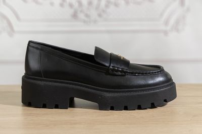 a close up of a black loafer shoe on a wooden table