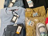 a pile of clothing that includes a pair of sneakers, a pair of jeans, a pair of pants, and a pair of shoes