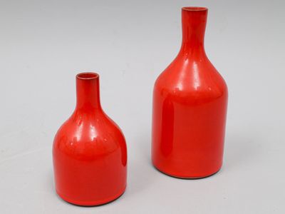 deux vases rouges posés l'un à côté de l'autre sur une surface blanche