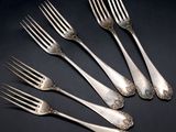 six silver forks with ornate designs on them on a black surface