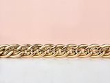 un gros plan d'un bracelet à chaîne dorée sur fond rose