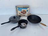 trois casseroles et poêles posées sur une table à côté d'un carton « Microwave Plus »