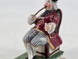 a figurine of a man sitting on a chair smoking a pipe