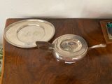 a silver tea pot and a silver plate on a wooden table