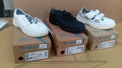 Trois paires de baskets blanches et noires sont posées sur un carton.