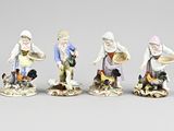 trois figurines représentant des personnes portant un chapeau et un tablier, posées sur une surface grise