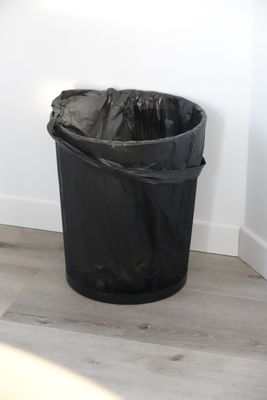 a black trash can sitting on the floor next to a white wall