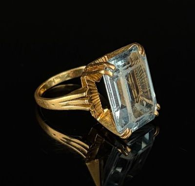 a gold ring with an emerald stone on a black surface