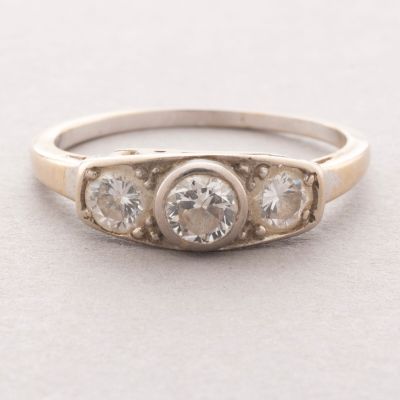un gros plan d'une bague en diamant à trois pierres posée sur une surface blanche