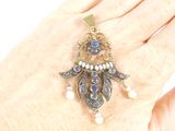 a woman ' s hand holding a brooch with a blue and white bead on it