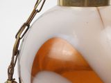 an orange and white glass lamp with a brass bell on a chain