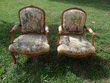 pair of antique chairs in the grass in front of a tree