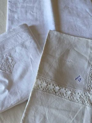three white linen napkins with embroidered designs on them sitting on a table