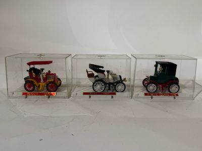 trois petites voitures dans une vitrine posée sur une surface blanche