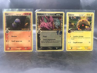 Trois cartes Pokémon sont posées sur une table.