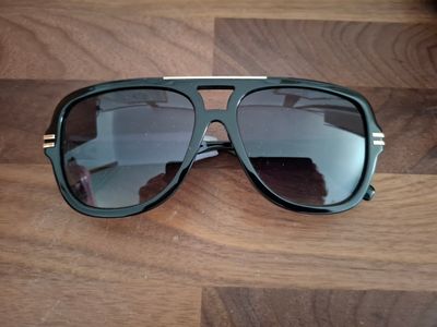 des lunettes de soleil noires posées sur une table en bois, sur laquelle se reflète le visage d'une personne