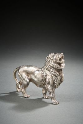 une figurine ancienne en argent représentant un lion, posée sur un support gris