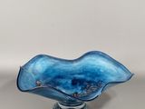 un bol en verre bleu posé sur un socle, sur une surface blanche